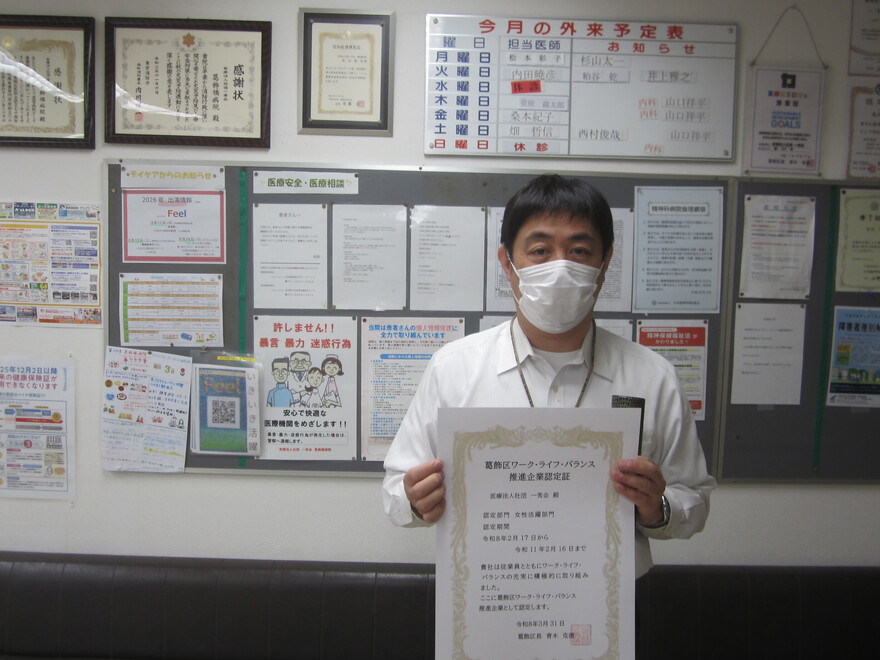 掲示板の前で代表が認定証を掲げている写真